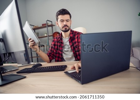 Photo of serious concentrated young man look laptop write hold tablet sit desk inside office indoors