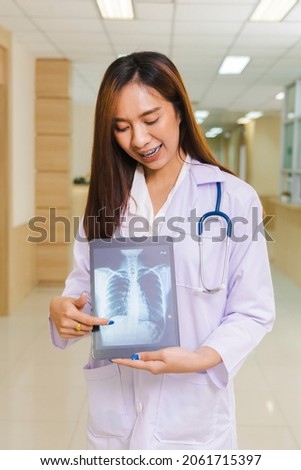 portrait of smart female doctor holding tablet to show X-Ray picture and standing at reception of the hospital.