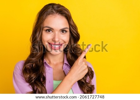 Portrait of attractive cheerful wavy-haired girl demonstrating copy empty space ad isolated over bright yellow color background