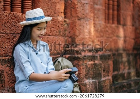 Young photographer female wearing hat sitting and checking photo in her camera while traveling in ancient site, she smile with happiness