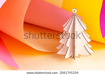 Bright wooden pink Christmas tree on colorful magenta and yellow paper swirls abstract background with copy space. Simple New Year and Xmas holidays template for greeting cards and winter decorations