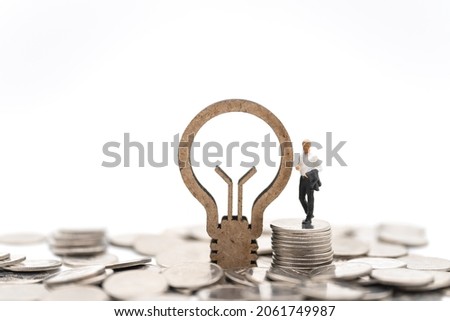Business, Financial and Idea Concept. Businessman miniature figure people standing on stack of silver coins with wooden lightbulb icon on white background.