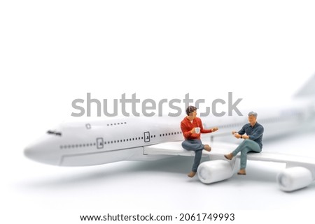 Travel Concept. Two man miniature figure people with cup of coffee sitting and talking on wing of airplane toy model on white background. Royalty-Free Stock Photo #2061749993