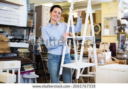 Smiling woman standing with stepladder in decoration and furniture store Royalty-Free Stock Photo #2061767318