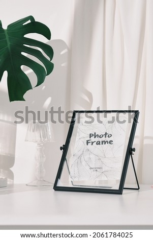 black and golden photo frame with color candles , glass lamp , glass flower pot with in white background and daylight , green leaf , home decoration photography