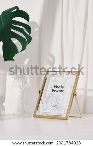 black and golden photo frame with color candles , glass lamp , glass flower pot with in white background and daylight , green leaf , home decoration photography