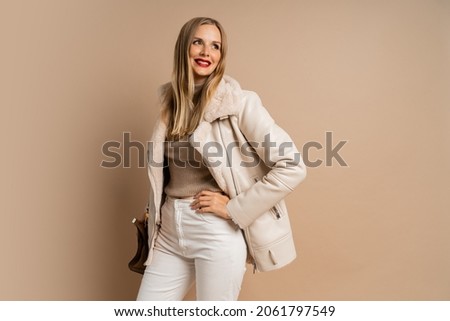 Winter studio fashion photo of elegant blond woman with red lips wearing trendy eco leather jacket , posing over beige background. 