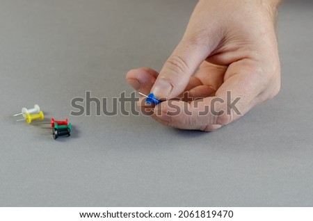 One Hand and push pins on gray background. Man with fingers holding one sharp thumbtack. Close-up. Selective focus. Royalty-Free Stock Photo #2061819470