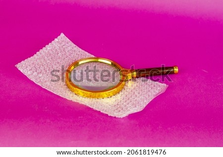 Magnifying glass and bubble wrap on pink background. Selective Focus.