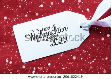 Label With German Calligraphy Frohe Weihnachten Und Ein Glueckliches 2022 Means Merry Christmas And A Happy 2022. Red Textured Background With Snowflakes
