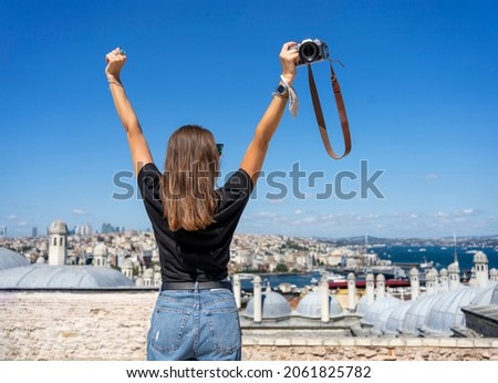 Back view of a photographer traveler woman wearing jeans and black t-shirt looking at the city view on a sunny day. 