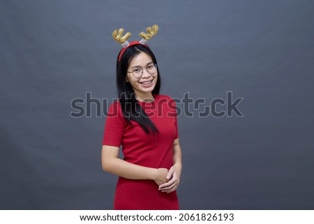 Portrait of an Asian woman wearing glasses in a beautiful red dress wearing and Christmas reindeer decorations antlers smiling