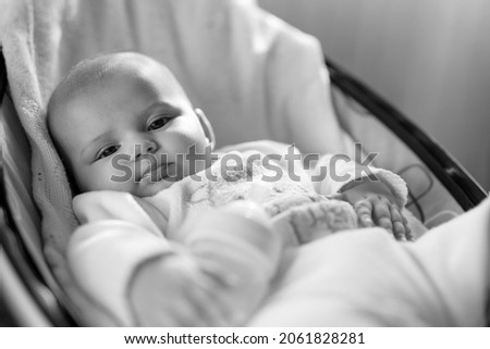 Cute baby laying in bouncer chair and sleep. Child relaxing in a swing with milk bottle. Adorable newborn baby in bodysuit. Family morning at home. Selective focus. Black and white photo. 