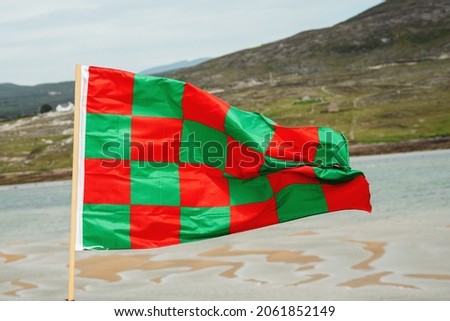Waving flag of county Mayo. Green mountain and cloudy sky in the background. Ireland.