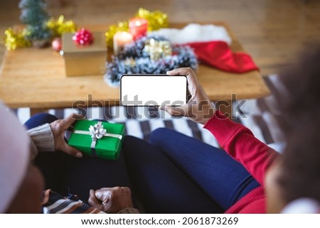 African american adult daughter and mother on christmas smartphone video call, copyspace on screen. christmas, festivity and communication technology at home.