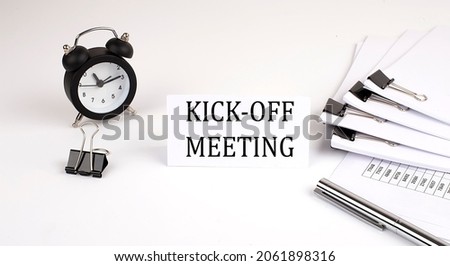 Card with text KICK OFF MEETING on a white background, near office supplies and alarm clock. Business Royalty-Free Stock Photo #2061898316