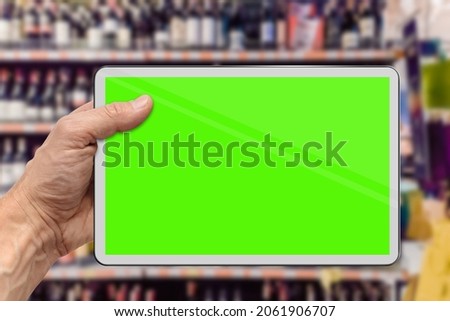 Man doing shopping at grocery store and scanning product with modern tablet, green chromakey screen