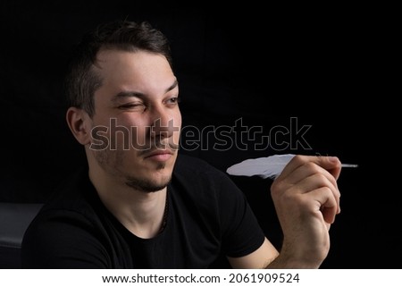 Young handsome man in black clothes with goose feather, dart metaphor close-up on a black background in low key. Goal setting concept