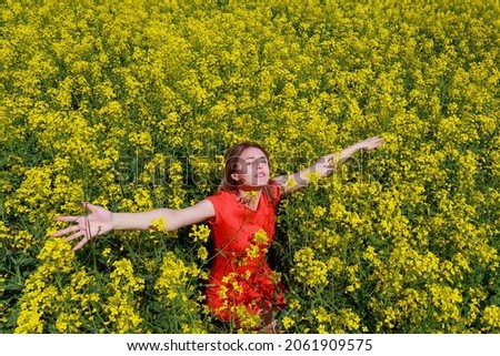 Young pretty woman in colored dress on lightning cheerful yellow background of blooming rapeseed field. Pleasure concept