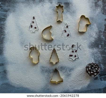 Golden Cookie Cutters for traditional Christmas cookies in the form of Santa Claus, a Christmas tree, a moon, an asterisk, a bell on a surface sprinkled with snow-white flour, next to a large cone.