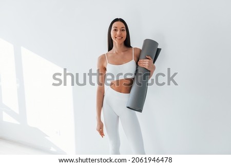 With mat in hands. Young caucasian woman with slim body shape is indoors at daytime. Royalty-Free Stock Photo #2061946478