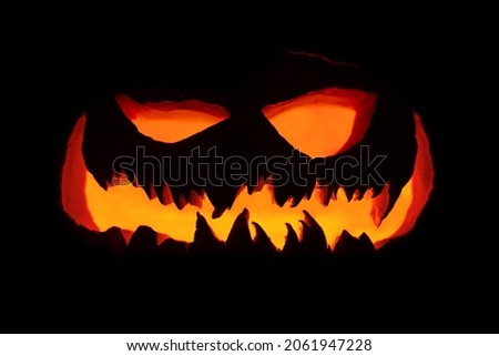 Smile of a maleficent pumpkin glowing from the dark, with warm tones on a dark background. Special for halloween with place for text