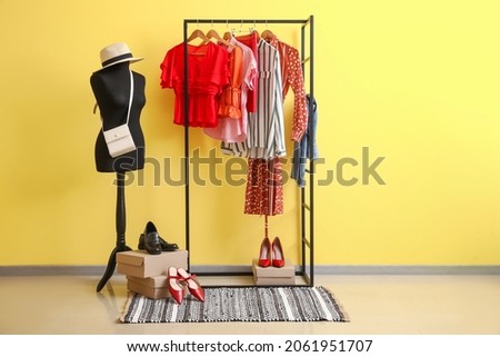 Rack with stylish clothes, shoes and accessories near color wall