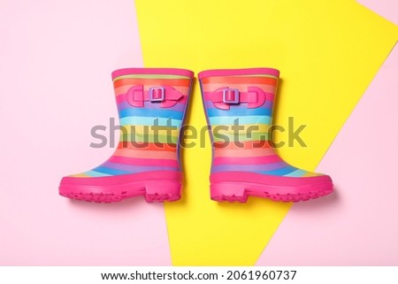 Pair of striped rubber boots on color background, top view