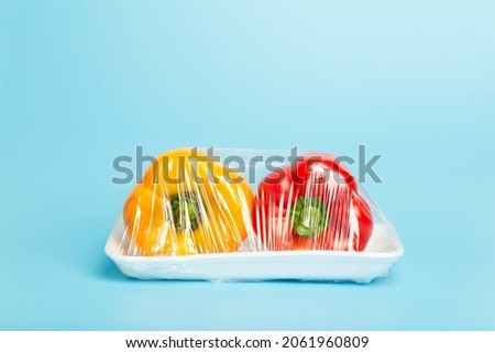 Vegetables in plastic packaging from the supermarket are minimal. Pepper in cellophane and non-degradable plastic on a blue background. Biodegradable product packaging, environmental protection Royalty-Free Stock Photo #2061960809