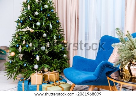 Stylish and modern New Year's interior of the room. In the kmnat there is a Christmas tree with gifts, a blue armchair, a table with New Year decor. Photo