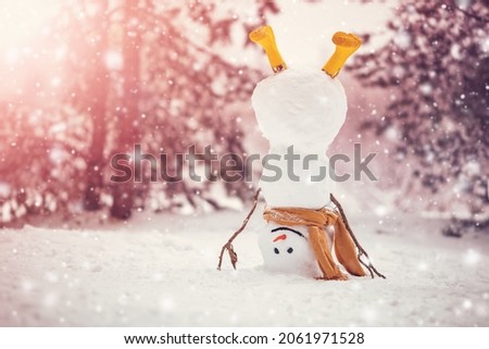 Cheerful snowman with orange scarf and in yellow boots stands upside down in winter forest Royalty-Free Stock Photo #2061971528