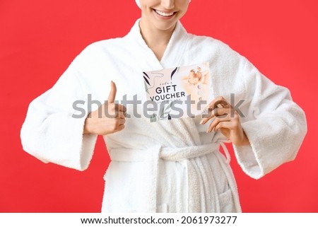 Young woman with gift voucher for massage showing thumb-up on color background