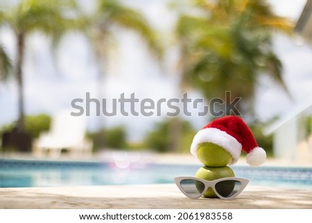 Snowman made of apples in a Christmas hat standing near swimming pool. Selective focus, blurred background.