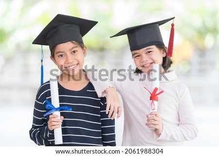 Two happy Asian female school kid graduates with a graduation cap holds a rolled certificate. Graduation Celebration Concept Stock Photo