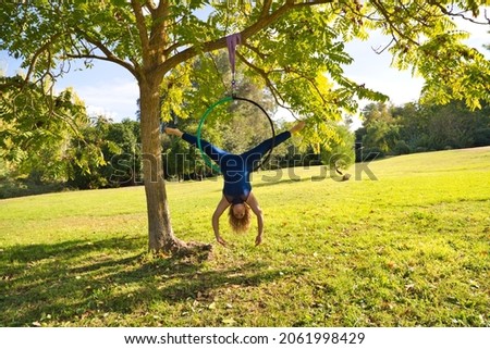 Blonde woman and young gymnast acrobat athlete performing aerial exercise on air ring outdoors in park. Lithe woman in blue costume performs poses of circus performers dancing with hips.