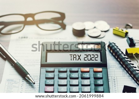 Word Tax 2022 on the calculator. Business and tax concept.Calculator, currency, book, tax form, and pen on wooden table.Top view. Royalty-Free Stock Photo #2061999884