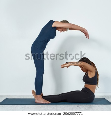 Vertical narrow shot of diverse multiethnic women in sportswear make G letter symbol training together. Sporty active multiracial females practice yoga pilates, have workout session. Sports concept.