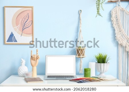 Laptop and wooden hand on table near color wall