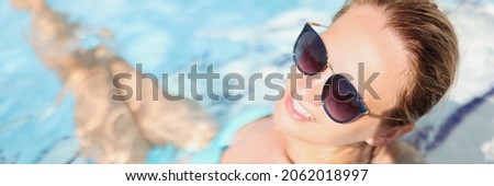 Young woman in blue swimsuit and sunglasses lying in pool and smiling