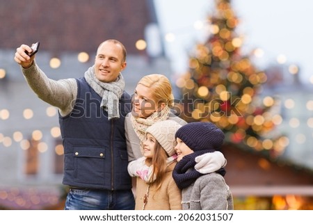 winter holidays, technology and people concept - happy family taking selfie with smartphone over christmas market background