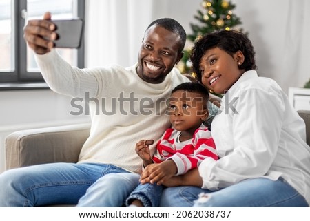 family, winter holidays and people concept - happy african american mother, father and little son taking selfie at home on christmas