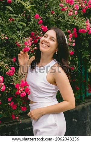 young pretty smiling woman near blooming red roses bush copy space