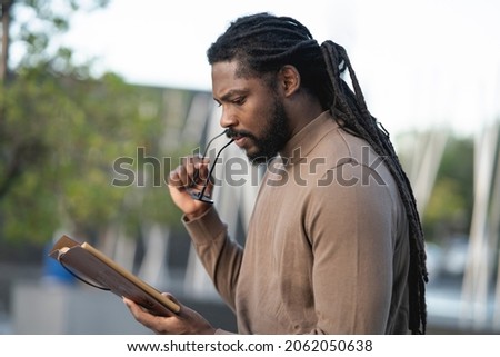African American man, with dreadlocks, and spectacles, reading a book at sunset Royalty-Free Stock Photo #2062050638