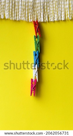 
Four wooden clothespins in various colors hung from each other, hung by a curtain on a yellow background.