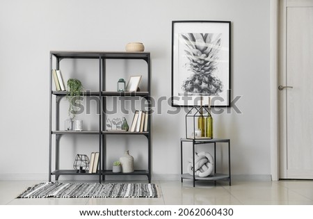Modern shelf unit with books and table near white wall in room