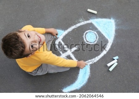 Child drawing rocket with chalk on asphalt, above view