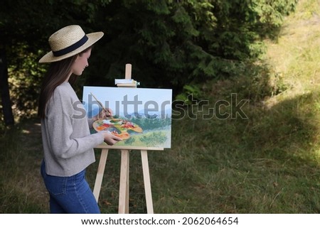 Young woman drawing on easel outdoors, space for text