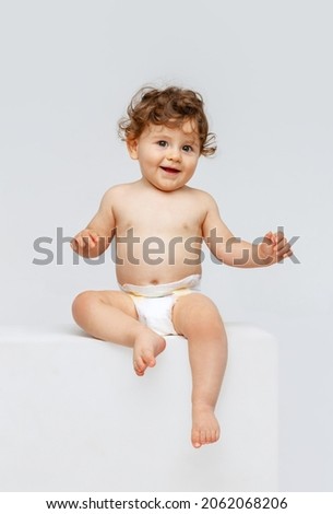 Smiling happy child. Portrait of little toddler boy, baby in diaper joyfully sitting and laughing isolated on white studio background. Concept of childhood, motherhood, life, birth. Copy space for ad Royalty-Free Stock Photo #2062068206