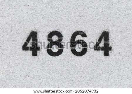 Black Number 4864 on the white wall. Spray paint. Number four thousand eight hundred and sixty four.