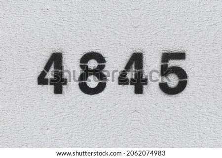 Black Number 4845 on the white wall. Spray paint. Number four thousand eight hundred forty five.